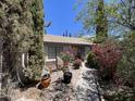 Charming home exterior, surrounded by lush trees, colorful flowers, and a stone-lined walkway at 6512 E Portia Cir, Mesa, AZ 85215