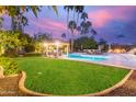 Expansive backyard with a sparkling pool, lush lawn, a cabana, and a cozy outdoor fire pit at 10658 E Cinnabar Ave, Scottsdale, AZ 85258