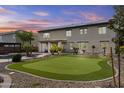 Expansive backyard featuring a lush green putting green, palm trees, and covered patio at 21337 E Waverly Dr, Queen Creek, AZ 85142