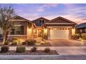 Charming single-Gathering home featuring a two-car garage, a stone facade, and illuminated landscaping at twilight at 20563 E Carriage Way, Queen Creek, AZ 85142