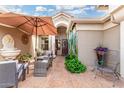 A cozy outdoor patio with comfortable seating under an umbrella, lush greenery, and a welcoming entrance at 16083 W Cambridge Ave, Goodyear, AZ 85395