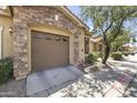Attached two car garage with stone accents, a paved driveway, and mature landscaping at 5415 E Mckellips Rd # 100, Mesa, AZ 85215