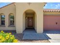 Close-up of home's entrance featuring an arched doorway, wooden door, and well-kept front yard at 14237 W Aster Dr, Surprise, AZ 85379