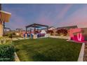 Backyard at dusk featuring artificial grass, pergola, outdoor kitchen, and lighted plants and fencing at 8127 E June St, Mesa, AZ 85207