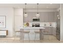 Bright kitchen with an island offering seating, stainless steel appliances, gray cabinetry and pendant lighting at 23443 W Albeniz Pl, Buckeye, AZ 85326
