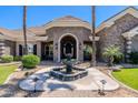 Close-up of the gorgeous front entrance with a stone archway, double doors, fountain, and manicured landscaping at 3949 E Norcroft Cir, Mesa, AZ 85215