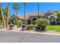 Attractive single-story stone home with lush landscaping, tall palm trees, and a circular driveway at 3949 E Norcroft Cir, Mesa, AZ 85215
