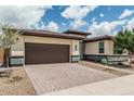 Single-story home showcasing a two-car garage with a brick-paved driveway and desert landscaping at 1272 W Camina Buena Vis, Queen Creek, AZ 85140