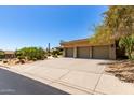 A large driveway leads to the three-car garage of this desert home, surrounded by mature landscaping at 16562 N 109Th Way, Scottsdale, AZ 85255