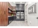 Modern laundry room with sleek cabinets, a wood accent wall, and dual front-load washer and dryer units at 22858 E Silver Creek Ln, Queen Creek, AZ 85142