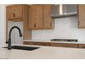 Close up view of sink, light countertops, wood cabinets, stainless vent hood, and gas cooktop at 10022 S 37Th Ave, Laveen, AZ 85339