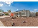 Charming home featuring desert landscaping with a red garage door and solar panels set beneath a bright sky at 6038 W Gelding Dr, Glendale, AZ 85306