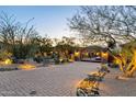 A desert landscaped driveway with an automatic gate leads to the beautiful home at dusk at 10092 E Troon North Dr, Scottsdale, AZ 85262
