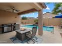 Inviting covered back patio with barbecue, ceiling fan, outdoor fireplace, and view of the refreshing pool at 41413 W James Ln, Maricopa, AZ 85138