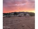 Expansive view of a large lot surrounded by a white fence under a vibrant sunset sky at 8678 S John Jacob Astor Ave, Casa Grande, AZ 85193