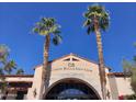 Exterior view of Corte Bella Golf Club's entrance, framed by tall palm trees against a clear blue sky at 12937 W El Sueno Ct, Sun City West, AZ 85375