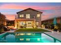 An outdoor oasis featuring a pool, fire pit, covered patio, and lush landscaping illuminated at dusk at 15711 S 11Th Ave, Phoenix, AZ 85045