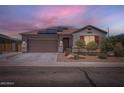 Inviting single-story home with a two-car garage, solar panels, and landscaped front yard under a vibrant sunset at 23730 W Hess Ave, Buckeye, AZ 85326