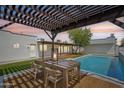 The backyard features a dining table under a pergola next to the sparkling pool, perfect for outdoor entertaining at 3043 E Hartford Ave, Phoenix, AZ 85032