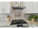 Close up of kitchen features stainless hood, cooktop, marble counters, and stylish geometric tile backsplash at 1070 S Amber St, Chandler, AZ 85286