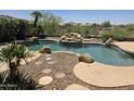 Inviting backyard pool with rock waterfall feature, lush landscaping, and a tranquil setting at 18359 W Sweet Acacia Dr, Goodyear, AZ 85338