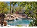 Beautiful pool with a stone waterfall feature, surrounded by lush landscaping and mature palms at 11717 E Estrella Ave, Scottsdale, AZ 85259
