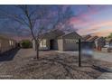 Charming single story home with desert landscaping and a two car garage underneath a vivid sunset sky at 16077 W Larkspur Dr, Goodyear, AZ 85338