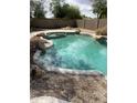 Backyard pool with natural rock features, surrounded by gravel and a privacy wall at 14228 N 150Th Ln, Surprise, AZ 85379