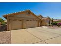 Tan single story home shows off its three-car garage and tidy desert landscaping at 8627 W Morrow Dr, Peoria, AZ 85382
