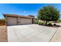 Well-manicured front yard featuring a three-car garage and lush, mature trees and shrubbery at 35654 N Vidlak Dr, San Tan Valley, AZ 85143