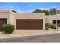 Two-car garage featuring a brown door, lush landscaping, and a paved driveway at 11633 N 40Th Way, Phoenix, AZ 85028