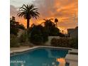 Relaxing pool area featuring lush landscaping, a mature palm tree, and a beautiful sunset at 3417 E Mission E Ln, Phoenix, AZ 85028