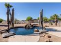 Backyard view of pool with rock waterfall feature, mature desert landscaping and shade umbrellas at 9998 W Prospector Dr, Queen Creek, AZ 85144