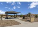 Shaded seating area in Magnolia Park, with picnic tables and a sign indicating the park's address at 18540 N Foxtail Dr, Maricopa, AZ 85138