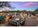 Inviting backyard with stone fireplace, seating, water feature, and desert landscaping illuminated at twilight at 30330 N 77Th Pl, Scottsdale, AZ 85266