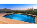 Inviting pool featuring pristine blue tile, stone accents, and stunning mountain views at dusk at 11550 E Paradise Ln, Scottsdale, AZ 85255