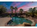 Backyard pool with rock features, palm trees, and string lights, perfect for outdoor entertaining at 11526 W Bermuda Dr, Avondale, AZ 85392