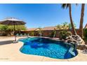 Beautiful backyard pool with a rock waterfall feature, an umbrella, and seating area at 8555 W Purdue Ave, Peoria, AZ 85345