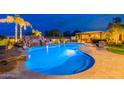 Gorgeous swimming pool area featuring a rock waterfall, lush landscaping, and an illuminated cabana at twilight at 27809 N Silverado Ranch Rd, Peoria, AZ 85383