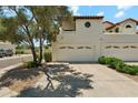 A three-car garage with white doors and a paved driveway, shaded by a mature tree and desert landscaping at 11011 N 92Nd St # 1005, Scottsdale, AZ 85260