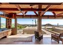 Covered patio showcases wooden beams, wet bar, stone counters, seating, and stunning mountain views at 8752 E Range Rider Trl, Mesa, AZ 85207