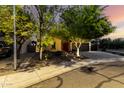 Beautiful single-story home with mature trees, desert landscaping, and warm lighting, creating an inviting ambiance at 17363 W Lisbon Ln, Surprise, AZ 85388