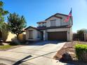 Two-story home featuring a two-car garage, neutral color scheme, manicured yard with tree, rock details and American flag at 19324 N Del Mar Ave, Maricopa, AZ 85138
