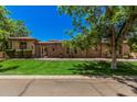 Stunning single-story stone home with lush green lawn and mature trees under a clear blue sky at 24348 S 201St Ct, Queen Creek, AZ 85142