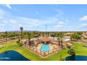 Aerial view of the community pool and clubhouse surrounded by palm trees and a serene pond at 10377 W Yukon Dr, Peoria, AZ 85382