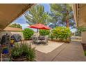 Relaxing back patio with a table and chairs set, an umbrella, beautiful yellow flowers, and lush greenery at 18626 N 130Th Ave, Sun City West, AZ 85375