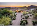 Expansive aerial view of estate with a circular driveway, lush desert landscaping, and mountain views at sunset at 11548 E Salero Dr, Scottsdale, AZ 85262