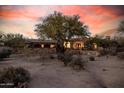 Stunning exterior view of a stone home featuring desert landscaping and a tree in front of a large arched window at 7552 E Whisper Rock Trl, Scottsdale, AZ 85266