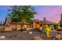 Single-story home with desert landscaping, rocks, and a mature shade tree at dusk at 5861 E Anderson Dr, Scottsdale, AZ 85254