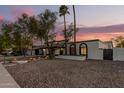 Inviting single-story home with desert landscaping, palm trees, and unique arched windows under a colorful dusk sky at 1736 N Ashbrook Cir, Mesa, AZ 85213
